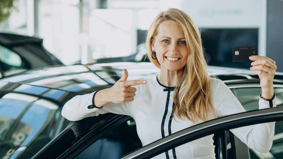 Eine Frau zeigt zufrieden auf die Ihre Bankkarte und freut sich über den besten Preis für ihr Auto